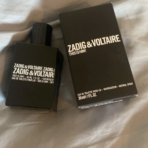 Zadig & Voltaire This Is Him! Eau de Toilette 30ml - En stilren svart parfymflaska från Zadig & Voltaire, 'This Is Him!' Eau de Toilette, 30 ml. Flaskan har en modern, kantig design med vit text och kommer med originalkartong. Doften är maskulin och passar dig som gillar unika och djupa toner. Testad en gång!