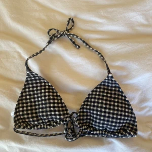 Svart och vit rutig bikiniöverdel från Tezenis - Säljer en snygg bikiniöverdel från Tezenis i svartvitt rutigt mönster. Klassisk trekantsmodell med knyt både i nacken och ryggen. Perfekt för sommardagar på stranden!
