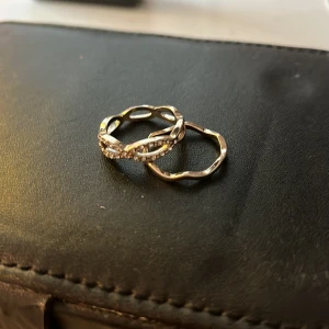 Två ringar i silverfärg - Säljer två snygga ringar, silverfärgade en med en vågig form och en med tvinnad design och glittriga stenar. Perfekta att bära tillsammans eller var för sig för en trendig look.‼️köp en för 10 kr och två för 20 kr‼️