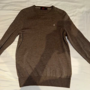 Brun stickad tröja från Morris - Säljer en klassisk brun stickad tröja från Morris med rund halsringning och diskret broderad logga på bröstet. Tröjan har långa ärmar och ribbade muddar vid ärmslut och nederkant. Perfekt för lager-på-lager-stil.