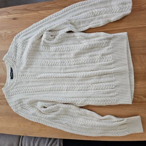 Vit stickad tröja med kabelmönster - Säljer en vit stickad tröja med klassiskt kabelstickat mönster. Tröjan har rund halsringning, långa ärmar och ribbade muddar vid ärmslut och nederkant. Perfekt för kyliga dagar och enkel att matcha med olika outfits.
