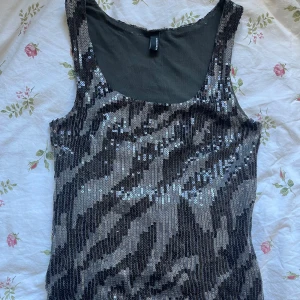 Zebramönstrad paljettopp i silver och svart - Säljer en glittrig zebramönstrad paljettopp i silver och svart. Toppen är ärmlös och har rund halsringning.