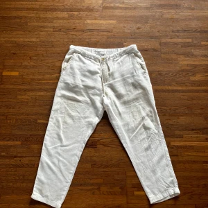 Vita linnebyxor - Säljer ett par crèmevita linnebyxor med normal passform. Byxorna har fickor fram och bak samt stängs med knapp och dragkedja. Perfekta för varma dagar och en stilren look.