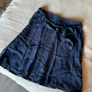 Mörkblå kjol med knyt från Vero Moda - Säljer en mörkblå kjol från Vero Moda i storlek XS. Kjolen har elastisk midja och ett snyggt knytband framtill. 
