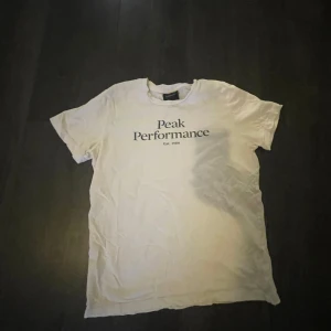 Vit t-shirt från Peak Performance - Vit t-shirt från Peak Performance med svart tryck på bröstet. Klassisk passform och rund halsringning. Perfekt för en clean och enkel stil. Köpt för 400kr. 