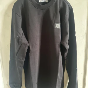 Svart långärmad sweatshirt från Stone Island - Säljer en svart långärmad sweatshirt från Stone Island med klassisk rund hals och ikonisk logotyp-patch på bröstet. Tröjan är i mjuk bomull och har en stilren, enkel design som passar till det mesta.