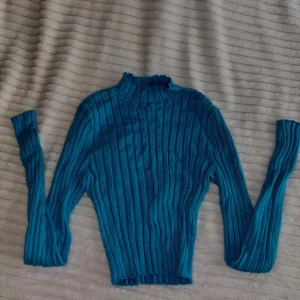 Turkos ribbad stickad tröja från FB Sister - Säljer en turkos ribbad stickad tröja från FB Sister. Tröjan har lång ärm, hög hals och är figurnära i modellen. Perfekt för att addera färg till din garderob!