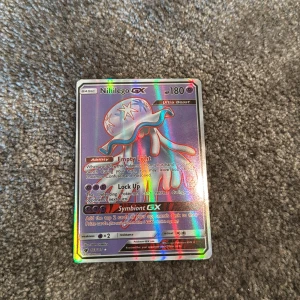 Nihilego GX Pokémonkort - Säljer ett holografiskt Nihilego GX-kort från Pokémon. Kortet har färgstark glansig yta och motiv av Ultra Beast Nihilego med 180 HP. Text och detaljer på engelska. Perfekt för samlare eller Pokémon-fans.