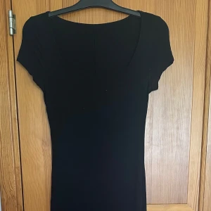 Svart långklänning med kort ärm - En stilren svart långklänning med rund halsringning och korta ärmar. Klänningen har en enkel och klassisk design som passar perfekt till olika tillfällen. Materialet känns mjukt och följsamt mot kroppen. (Hela fick inte plats på en bild)
