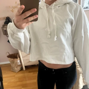 Vit croppad hoodie - Säljer en vit croppad hoodie med huva och dragsko. Tröjan har långa ärmar och en avslappnad passform. Perfekt för en casual look och enkel att matcha med jeans eller leggings.
