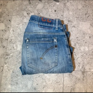 Blå jeans från Dondup - Säljer ett par klassiska blå jeans från Dondup, modell George. Jeansen har normal passform, fem fickor och snygga slitningar för en avslappnad look. Pris är diskuterbart vid snabb affär. Inga defekter men hål vid knäna som är designen.