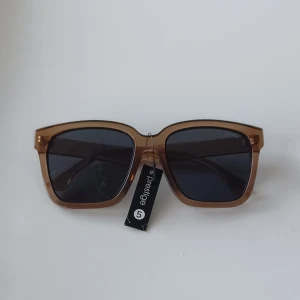 Bruna solglasögon från Prestige - Snygga solglasögon från Prestige 5 med fyrkantig form och transparent brun båge. Glasen är mörka och ger ett coolt intryck. Perfekt accessoar för att lyfta din stil under soliga dagar.