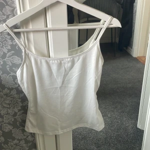 Vit linnetopp med smala axelband - Säljer en enkel och stilren vit linnetopp med smala axelband. Perfekt att matcha med jeans eller kjol för en fräsch look. Toppen är i mjukt material och har en klassisk rak passform.