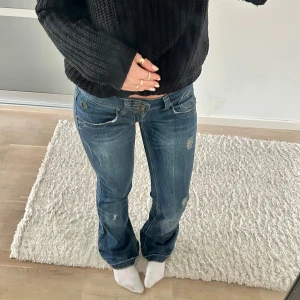 Blå bootcut jeans med slitningar - Säljer ett par blå bootcut jeans med slitna detaljer. Jeansen har låg midja och klassisk femficksdesign. Perfekta för en avslappnad och trendig look. Dom är uppsprättade nertill och därav lite slitningar (sista bilden)