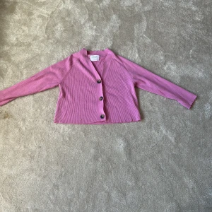 Rosa ribbad kofta från Zara - Säljer en rosa ribbad kofta från Zara med tre knappar framtill. Koftan har lång ärm och är croppad i modellen. Perfekt att slänga över en topp för en snygg lager-på-lager-look.