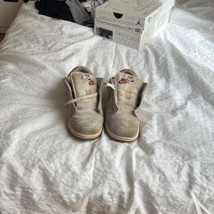 Nike Dunk Low med röd swoosh - Nike Dunk Low sneakers i beige med röd swoosh och vita detaljer. Skorna har snörning, rund tå och platt sula. Perfekta för dig som gillar klassisk streetwear-stil och vill ha något som sticker ut lite extra. Har ingen sko box