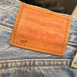 Levi's 501 ljusblå jeans - Klassiska Levi's 501 jeans i ljusblå tvätt med raka ben och femficksdesign. Jeansen har den ikoniska läderpatchen bak i midjan och röd Levi's-tagg på bakfickan. Perfekta för en avslappnad och tidlös stil.