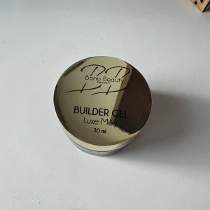 Builder Gel Luxe Milky från Bano Beauty - Builder Gel Luxe Milky från Bano Beauty i en lyxig burk på 30 ml. Gelen har en mjölkig, ljusrosa nyans och används för att bygga och förstärka naglar. Perfekt för dig som vill skapa en naturlig och elegant look på naglarna. Tyvärr en liten defekt på burkens utsida vilket syns på bilden men inget som påverkar. Testad en gång🥰