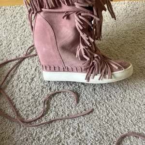 Rosa mockasneakers med fransar och kilklack - Säljer ett par unika rosa sneakers i mocka med kilklack och massor av fransdetaljer. Skorna har snörning och vit platt sula, perfekt för dig som vill sticka ut med din stil och vill vara trendig. Säljer för att de tyvärr var lite för små.