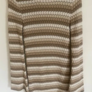 Beige och vit randig stickad klänning från Somethingnew - Säljer en stickad klänning från Somethingnew i beige och vitt med horisontella ränder. Klänningen har lång ärm och ett diskret hålmönster i stickningen.