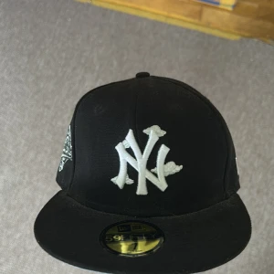 Svart New Era 59FIFTY keps med NY-logga - Säljer en svart New Era 59FIFTY keps med vit broderad New York Yankees-logga framtill och World Series-märke på sidan. Klassisk passform och MLB-logga baktill. Perfekt för dig som gillar streetwear och sportig stil.