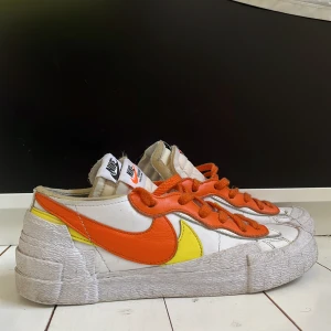 Nike Blazer Low med orange och gul detalj - Nike Blazer Low sneakers med vit bas, orange swoosh och snörning samt gula detaljer på sidan. Skorna har en chunky, texturerad sula och dubbla tungor med Nike-logga. Perfekta för dig som gillar färg och unik design. Dem skickas i original lådan. Pris kan definitivt diskuteras, bara att komma pm! Nypris ca 1350kr