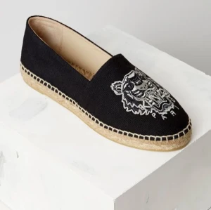 Svarta Kenzo espadrillos  - Svarta espadrillos från Kenzo med broderad tiger på ovansidan. Skon har en rund tå och en klassisk flätad sula i naturfärgat material. Perfekt för dig som vill ha en stilren men ändå unik sko. 🌟🥰Aldrig använda💖Nypris ca 2000 kr