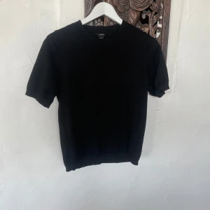 Svart t-shirt från Lindex - En klassisk svart t-shirt från Lindex med rund hals och korta ärmar. T-shirten har en enkel och stilren design, perfekt att matcha med allt. Materialet känns mjukt och bekvämt mot huden.