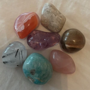 Samling av sju polerade kristaller och stenar - Säljer ett set med sju olika polerade kristaller och stenar. Innehåller bland annat en rosa rosenkvarts, en blågrön amazonit, en lila ametist, en brun tigeröga, en orange agat, en vit sten med svarta streck och en beige sten. Perfekt för dig som gillar kristaller och mineraler. (Vet ej om dom är äkta) säljer alla för 50 eller 10kr styck