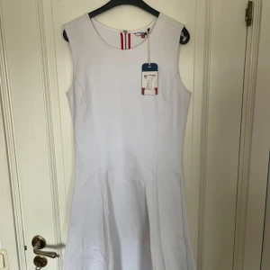 Vit ärmlös klänning från Tommy Hilfiger - Säljer en helt oanvänd stilren vit ärmlös klänning från Tommy Hilfiger med diskret logga nertill och dragkedja i ryggen. Klänningen har en klassisk, något utställd passform och är perfekt för sommarens tillfällen.