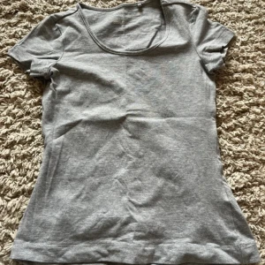 Grå basic t-shirt från Esmara - Enkel grå t-shirt från Esmara med rund halsringning och korta ärmar. Tillverkad i mjuk bomull, perfekt för en avslappnad stil. Passformen är normal och materialet känns skönt mot huden.