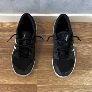 Svarta skor från Asics - Säljer ett par svarta Asics sneakers med vita detaljer och logga på sidan. Skorna har snörning och en platt, vit sula. Perfekta för träning eller vardagsbruk. Klassisk sportig design med bekväm passform. Nypris=899kr, Mitt pris=130kr! Pris kan diskuteras. Vid frågor kring prudukten så är det bara att dma oss😊. M.V.H./////////. Avn Closet🍾🍾🍾