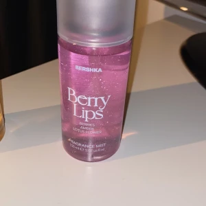Berry Lips Fragrance Mist från Bershka - En rosa doftmist från Bershka med namnet Berry Lips. Doften har inslag av bär, amber och lotusblomma. Flaskan är genomskinlig med glittereffekt och rymmer 150 ml. Perfekt för dig som gillar fruktiga och blommiga dofter.