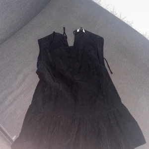 Svart blus  med struktur - Säljer en svart ärmlös blus med lätt v-ringning och knytning i nacken. Blusen har en subtil prickig struktur i tyget och en volang nedtill som ger extra rörelse. Perfekt för dig som gillar en enkel men ändå detaljrik look. Den är endast använd 2 gånger och har inga fel. Passar storleken S skulle jag säga än xs.