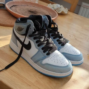 Nike Air Jordan 1 High OG University Blue - Säljer ett par Nike Air Jordan 1 High OG i färgen University Blue. Skorna har vit tå och sidor, ljusblåa paneler och svart swoosh samt svarta skosnören. Klassisk hög modell med perforerad tå och ikonisk Jordan-logga vid ankeln. Knappt andvända och mycket bra skick. Tyvärr ingen box och inget kvitto. Äkta!