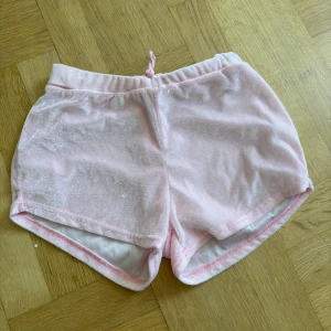 Ljusrosa mjuka shorts i frotté - Säljer ett par ljusrosa shorts i mjuk och glansig frotté med resår och knyt i midjan. Perfekta för sommardagar eller som mysplagg hemma. De har en avslappnad passform och är riktigt bekväma. Lite svarta fläckar på sista bilden men går nog få bort 