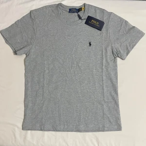 Grå t-shirt från Polo Ralph Lauren - Snygg grå t-shirt från Polo Ralph Lauren med klassisk passform och liten broderad logga på bröstet. Perfekt basplagg med rund hals och korta ärmar. Stilren och enkel att matcha till allt.