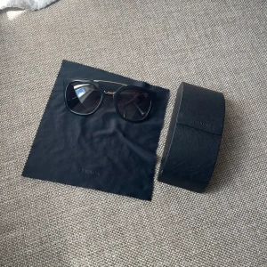 Svarta solglasögon från Prada med gulddetaljer - Snygga svarta solglasögon från Prada med markerad båge och guldfärgade metallskalmar. Glasögonen har en modern, oversized form och kommer med originalfodral och putsduk. Jätte bra skick nästan aldrig använda!