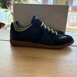 Mörk blåa Maison margiela - Säljer ett par mörkblå skor från Maison Margiela med ovandel i mocka och skinn, vita snören och klassisk gummisula. Storlek 43 men passar 44! Allt OG innehåller också! Kom med frågor och funderingar.