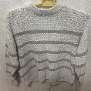 Beige och vit stickad tröja med ränder - Mysig stickad tröja från lager 157 i beige och vitt med horisontella ränder. Tröjan har en rund halsringning och långa ärmar. Perfekt för kyligare dagar och enkel att matcha med jeans eller kjol.