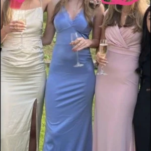 Ljusblå balklänning med spetsdetaljer - Säljer en ljusblå långklänning med smala axelband som korsas i ryggen och fina spetsdetaljer längs urringningen. Klänningen har en figurnära passform och är tillverkad i ett glansigt material som ger en elegant look. Klänningen är uppsydd nertill för att jag inte ville att den skulle släpas i marken och uppsydd lite vid bysten av en sömmerska. Jag är (175cm) 