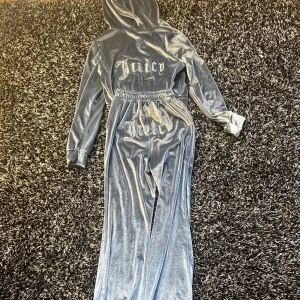Juicy Couture mjukisbyxor i grå sammet - Juicy Couture mjukisbyxor i glansig grå sammet med resår i midjan och breda ben. Klassisk logga på baksidan. Perfekta för en avslappnad och trendig look. Ej äkta 