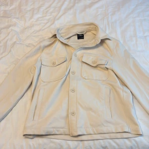 Beige overshirt från ZARA - Säljer en beige overshirt från ZARA med klassisk krage och knäppning framtill. Jackan har två bröstfickor med lock och knappar samt två sidofickor. Perfekt för lager-på-lager och enkel att styla.