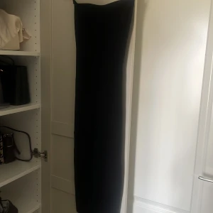 Svart långklänning med axelbandslös design - Bandeau klänning från Gina. Storlek M men mer som S. Aldrig använd. Den har en liten slits där bak också 