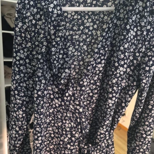 Blommig omlottklänning från ONLY - Mörkblå omlottklänning från ONLY med vitt blommönster. Klänningen har långa ärmar och knyt i midjan för en smickrande passform. Perfekt för vår och sommar!