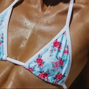Blommig trekantsbikini från Bright Swimwear  - Säljer en söt trekantsbikini från Bright med blommigt mönster i rosa och grönt på ljusblå botten. Bikinin har vita kanter och knytband i nacken och ryggen. Tyvärr var den för liten för mig, men säljer den för det pris som jag köpte den för på rean 😍💞liten i storleken 