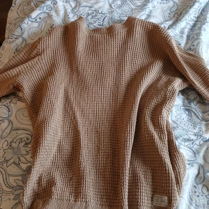 Beige stickad tröja från 157 - Säljer en beige stickad tröja från 157 med grov ribbad struktur. Tröjan har lång ärm och en avslappnad passform, perfekt för lager-på-lager. Enkel och stilren design utan synliga detaljer.