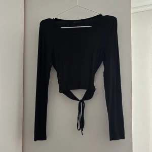 Svart långärmad croppad topp med knyt - Säljer en svart långärmad topp med croppad passform och knyt backtill. Toppen har en rund halsringning och är tillverkad i ett stretchigt material som sitter snyggt på kroppen. Perfekt till jeans eller kjol.
