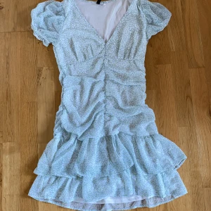 Ljusblå/ljusgrön blommig volangklänning  - Supersöt ljusblå kortklänning med småblommigt mönster och volanger från H&M Divided. Klänningen har v-ringning, korta puffärmar och rynkade detaljer framtill. Perfekt för sommarens alla tillfällen!