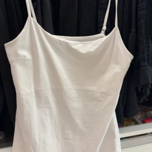 Vit linnetopp med smala axelband - Säljer en enkel och stilren vit linnetopp med smala justerbara axelband. Perfekt att matcha med jeans eller kjol för en fräsch look. Toppen är i mjukt material och har en rak passform.